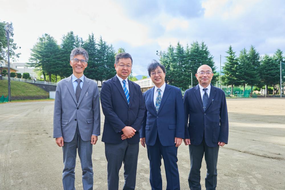 山梨県立富士河口湖高等学校グラウンドでの写真。左から渡邊総務主任、加藤校長、青木教授、石原教頭